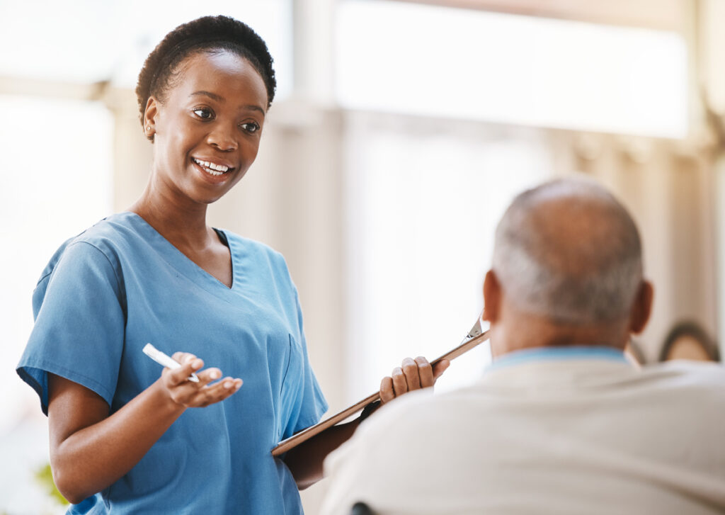 Nurse in blue scrubs with clipboard talking with patient